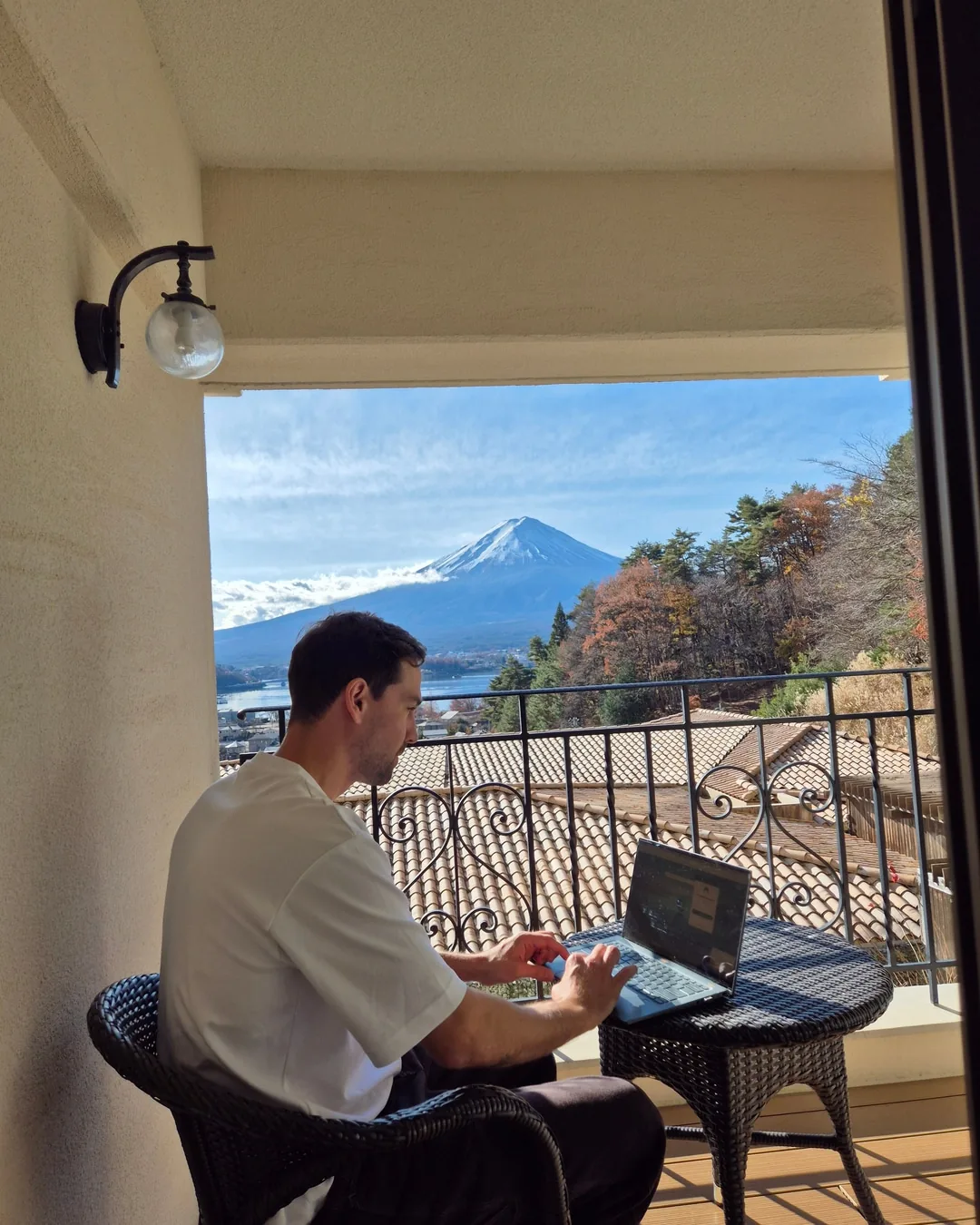 Aaron working on a laptop on a balcony, Mount Fuji behind him